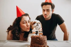 Pareja y su perro apagando las velas de un pastel en el cumpleaños de la mascota